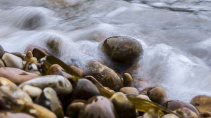 Close up of pebbles on the coast of the ocean with a wave coveri