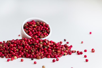 Pink pepper pile on white desk and white bowl. Closeup. Copy space.