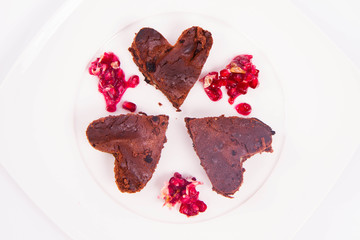 Heart shaped slices of a brownie decorated with pomegranate on white background