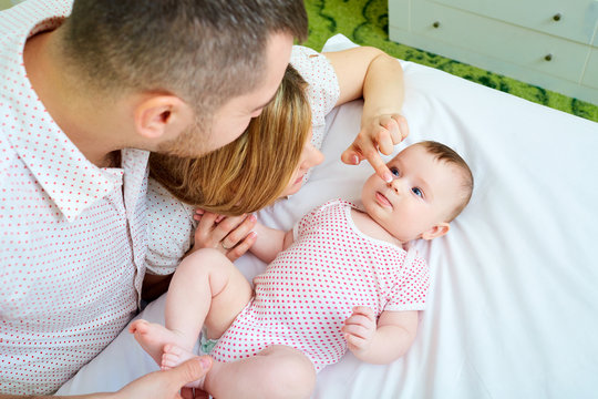Baby with his mother and father on the bed playing together. Happy family at home.
