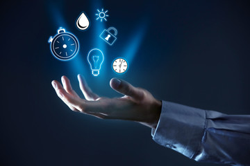 Business and time management concept. Male hand holding icons on dark background