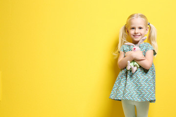 Cute little girl with bunny toy on color background