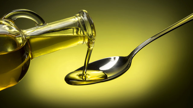 bottle pouring oil in a spoon on green background