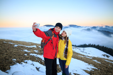 Young couple hiking outdoors with backpacks in winter mountains. Happy traveling couple making selfie