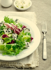 Green salad with spinach, frisee, arugula, radicchio, feta cheese and black sesame seed on blue wooden background