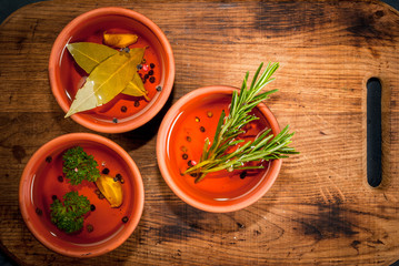 Selection of scented oils from herbs and spices: rosemary, garlic, pepper, parsley, bay leaf. On a dark gray stone kitchen table. Top view, copy space
