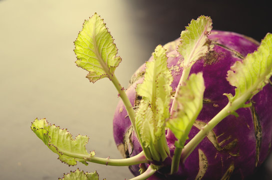 Purple kohlrabi cabbage with green leaves on dark wooden table