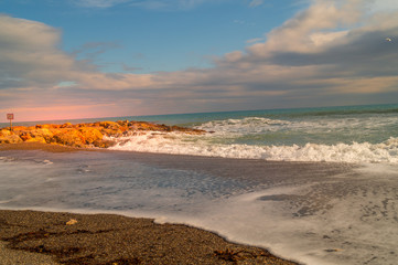 Fototapeta na wymiar sea landscape. Beach with waves and rocks, sky with clouds and sun. Sunset on beach