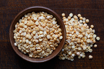 Dry yellow split peas in brown wooden bowl isolated on dark wood.