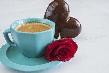 holiday concept/blue cup of coffee,red rose flower and chocolate heart on white wooden background