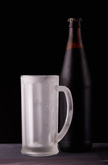 Dark beer in bottle and empty frost-coated mug.