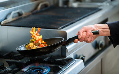 Koch oder Küchenchef wendet Gemüse in Pfanne in professioneller Küche