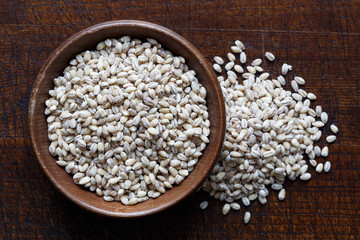 Dry pearl barley in brown wooden bowl isolated on dark wood.