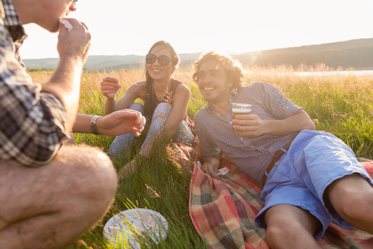 Junge M&auml;nner und Frauen sitzen zusammen im Gras und essen Hamburger auf einer Grillparty auf Wiese