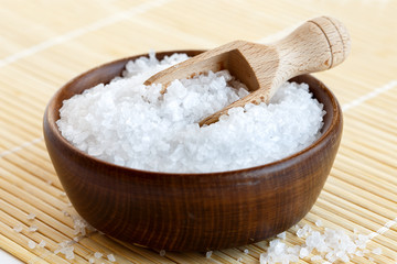 Rock salt in wooden bowl with wooden spoon on bamboo matt.
