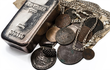 Silver bullion, antique silver and bronze coins and jewelry lying on old banknotes. On a white background.