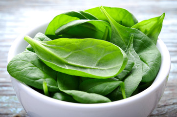 Fresh Baby spinach leaves in white bowl on blue wooden background. Top view with copy space,...