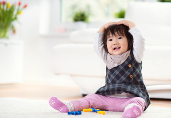 Pretty happy little japanese girl playing on capet at home