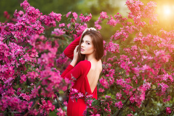 Obraz na płótnie Canvas Spring touch. Happy beautiful young woman in red dress enjoy fresh pink flowers and sun light in blossom park at sunset.