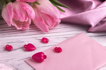 Valentine's day background with pink tulip flowers red hearts shape sign on white pink envelope on white wooden background.