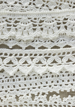 Handmade crocheted cotton organic lace ribbons on linen background. White original organic crochet frame, Knitted pattern backdrop with handicraft work, Mori Girl lace style. Creative craft