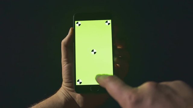 Closeup of young man hands typing sms scrolling pictures phone. Night. Green screen. Chroma key.