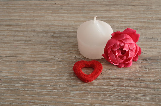 A white candle, a pink rose and a red heart