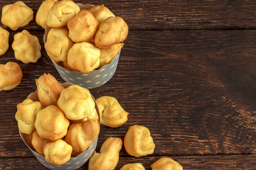 Sweet eclairs or profiterole in gray paper cups with stars on wooden background. French dessert. Empty space for design text template.