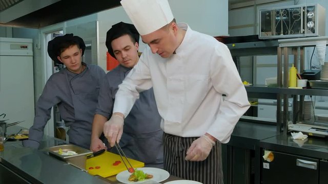 Chef learning his trainees how to decorate shrimp salad on a white plate