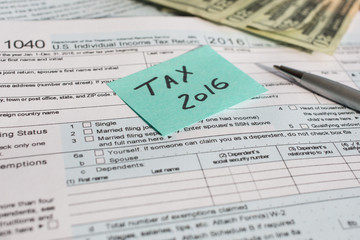 A shot of US Income Tax time 2016 written on a written on a bright sticker and  tax form 1040 with pen and twenty dollars banknotes US 1040 tax form