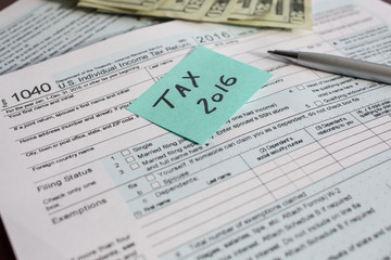 Fototapeta premium Tax time 2016 written on a written on a bright sticker and tax form 1040 with pen and twenty dollars banknotes US 1040 tax form