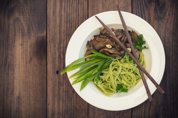 Plate of spaghetti dough with spinach and oyster mushrooms. Italian cuisine, Italian recipes. Wooden background. Top view. Close-up