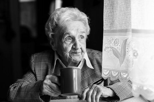 Elderly woman drinking coffee, black and white portrait.