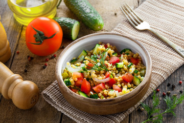 Traditional Israeli healthy meal Ptitim with tomatoes, cucumber and onion for delicious healthy breakfast. Classic Moroccan couscous with vegetables. Top view.