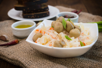 Braised cabbage with carrots and mushrooms in a bowl. Wooden background. Top view. Close-up
