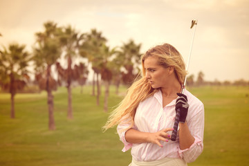 Fashion sport style beautiful woman standing holding golf club on outdoors green field background