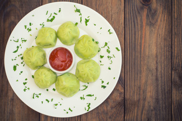 Georgian dumplings Khinkali of spinach dough with meat and tomato spicy sauce satsebeli. Wooden background. Top view. Close-up