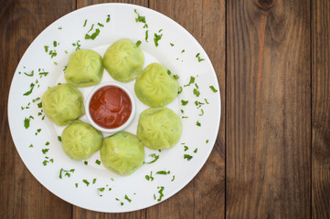 Georgian dumplings Khinkali of spinach dough with meat and tomato spicy sauce satsebeli. Wooden background. Top view. Close-up