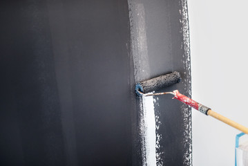 construction worker painting gray walls using paint roller. Details of interior design, renovation and plastering walls..