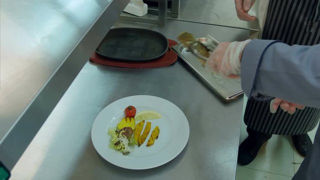 Chef explaining cook trainee how to put fish on a plate with vegetables