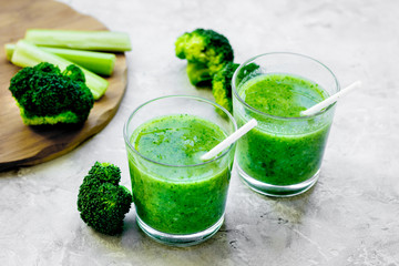 Green vegetable smoothie in glass at gray background