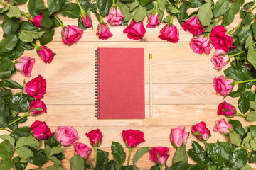Fresh pink rose flower and empty white note book on wooden deck.