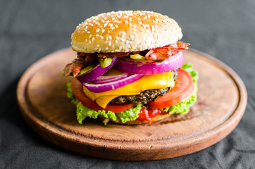 Burger on a wooden table against black background. Selective focus