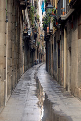 Fototapeta na wymiar A narrow alley with puddles after a downpour in Barcelona, Spain