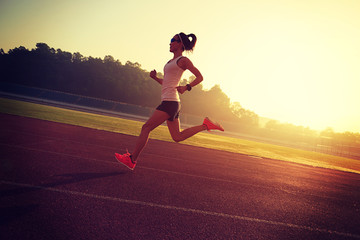Fototapeta na wymiar Young woman running during sunny morning on stadium track