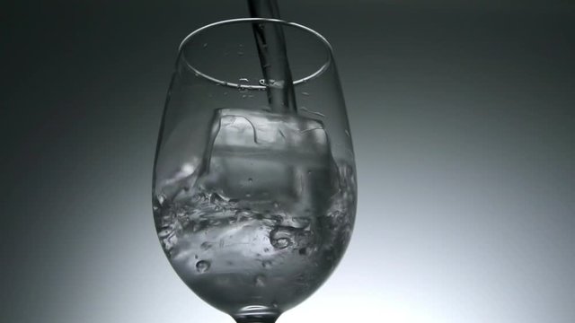 Pouring water into glass with ice cubes, slow motion.