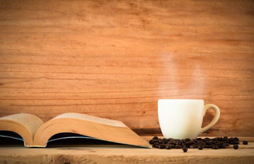 the book and hot coffee in white cup with black coffee bean on wood table