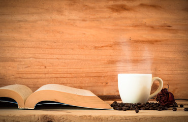 the book and hot coffee in white cup with dried red rose flower