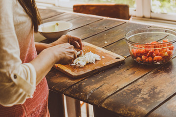 Mujer cortando cebolla con cuchillo en una table de madera antigua.