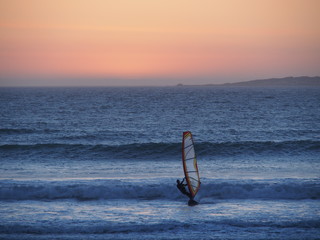Ocean sunset, windsurfer silhouette sailing against a sunset background.